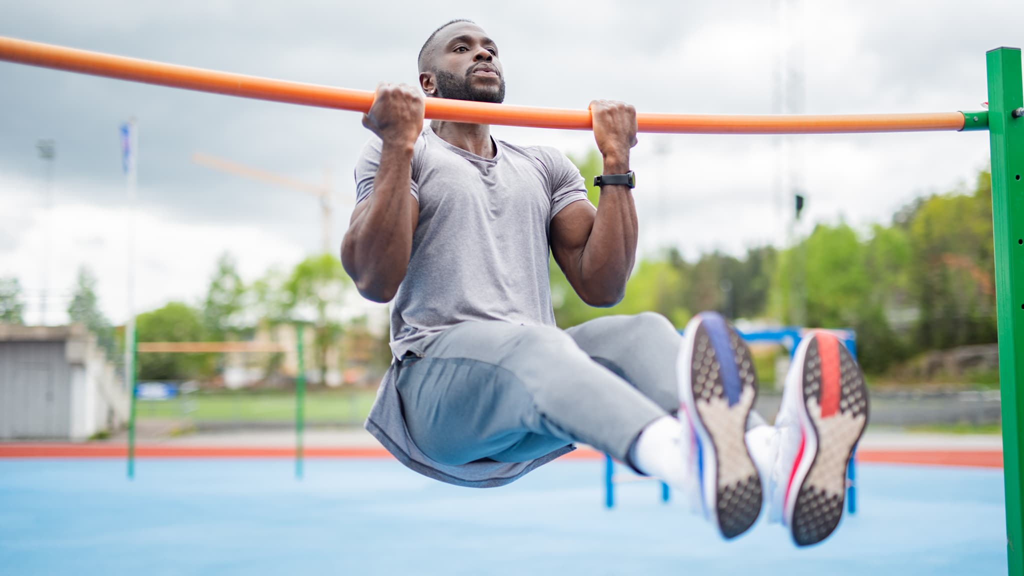 A photo of a man outside wearing gym clothes completing a pull-up using an outdoor pull-up station.
